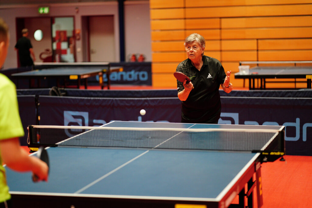 Ältere Frau spielt Tischtennis in einer Sporthalle