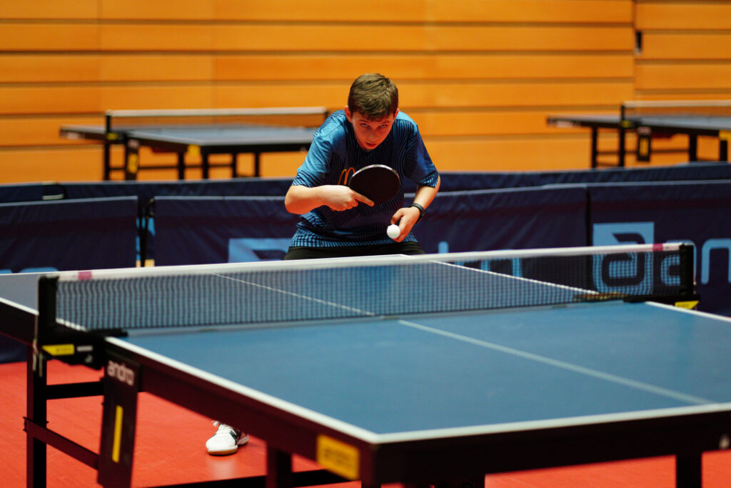 Junger Mann spielt Tischtennis in einer Halle