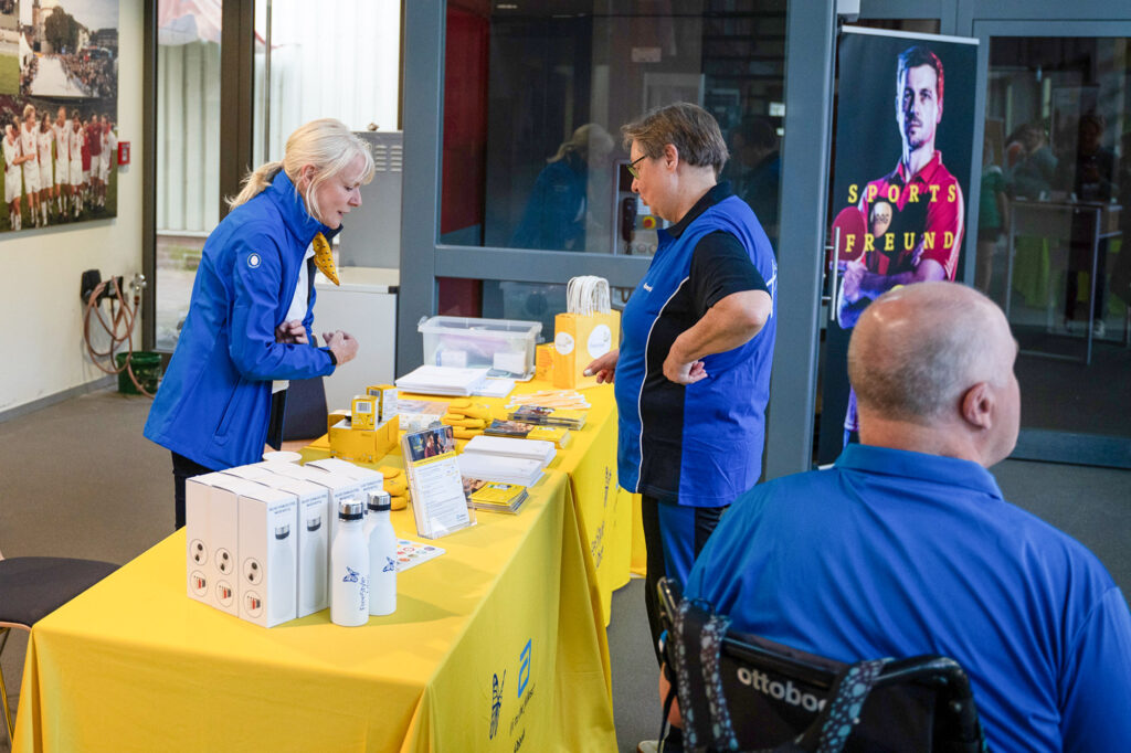 Menschen an einem Informationsstand mit Werbematerialien und Rollstuhlfahrer