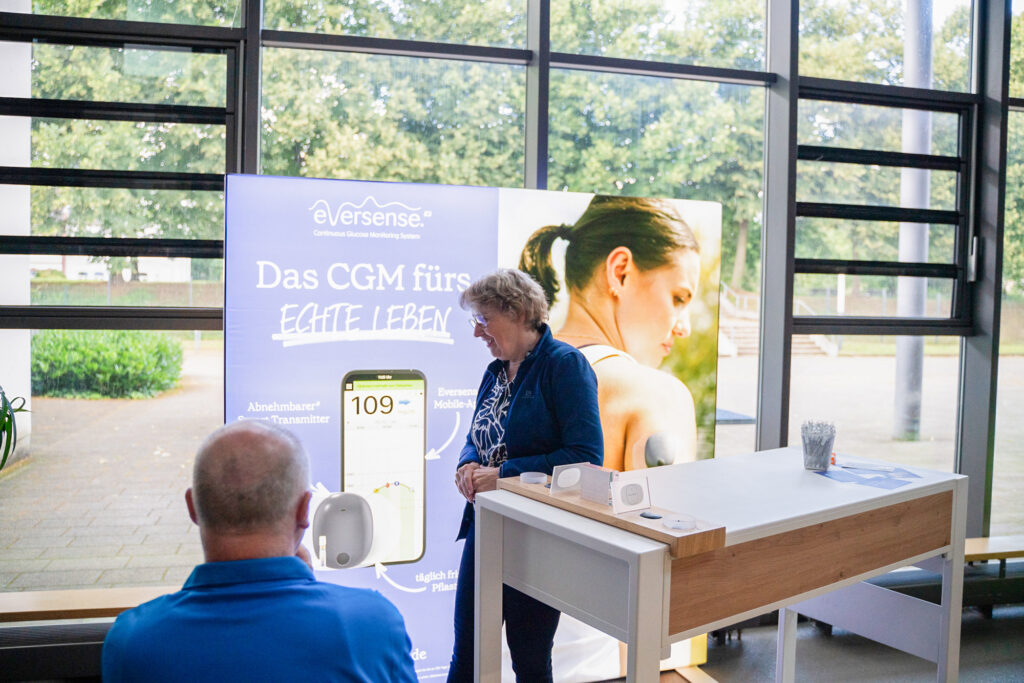 Frau präsentiert Gerät vor Eversense Poster in Meetingraum